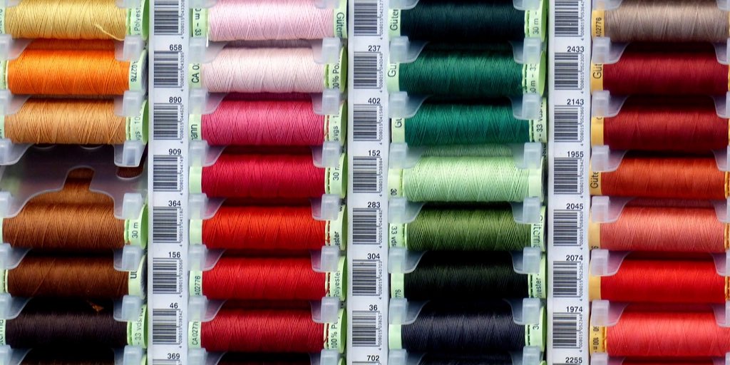 Rijen klosjes garen in alle kleuren, op een rij in een bak